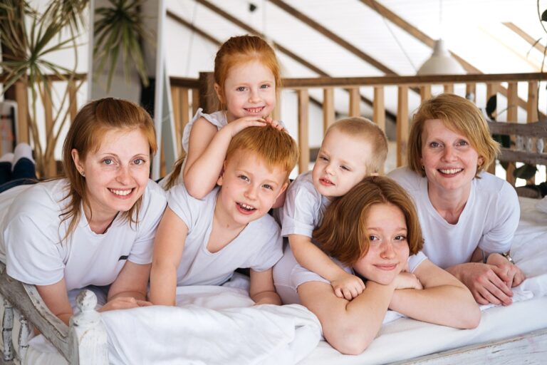 Two sisters with children lie on the bed. Red-haired women and their children. Great genetics.